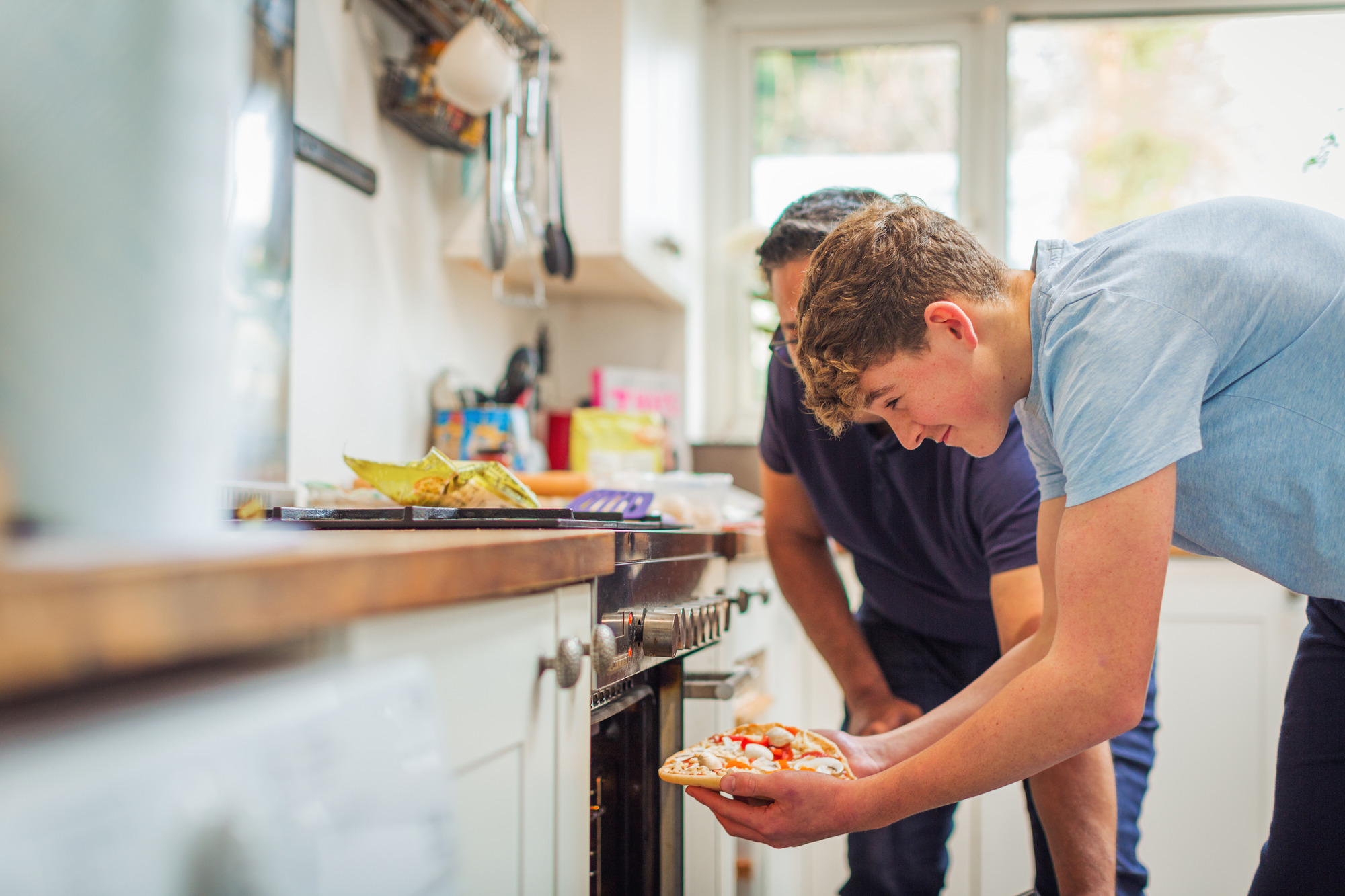 father and son putting pizza in the oven